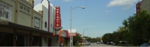 Main street with vintage storefronts and a tall red HEIGHTS sign against a blue sky, cars parked along the road.