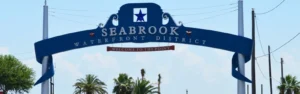 Blue decorative arch sign reading 'Seabrook Waterfront District' with a small 'Welcome to the Point' banner, palm trees in the background.