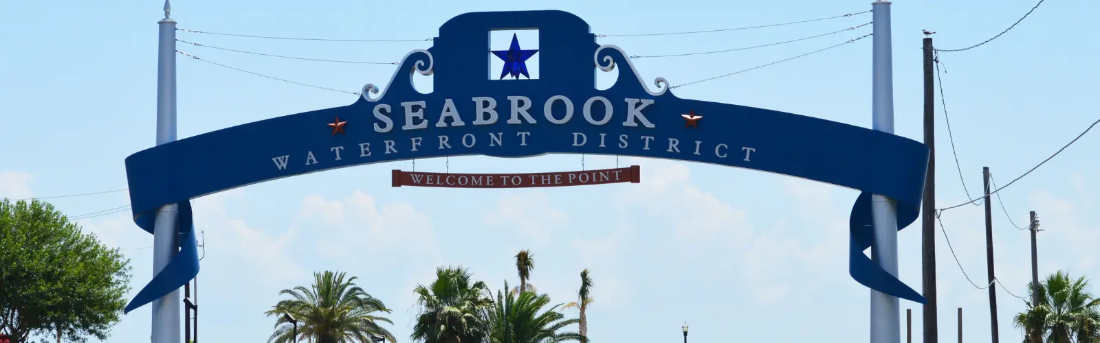 ac-repair-in-seabrook-texas | Castle AC & Heating Blue decorative arch sign reading 'Seabrook Waterfront District' with a small 'Welcome to the Point' banner, palm trees in the background.