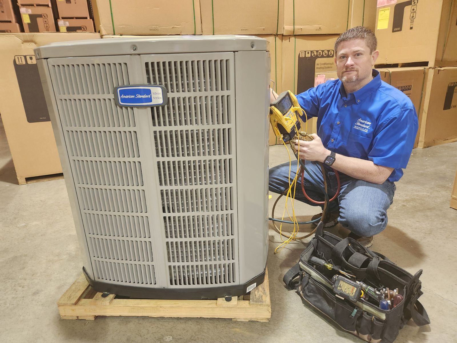 Castle AC and Heating owner Josh Cartwright with refrigerant gauges beside an American Standard outdoor unit