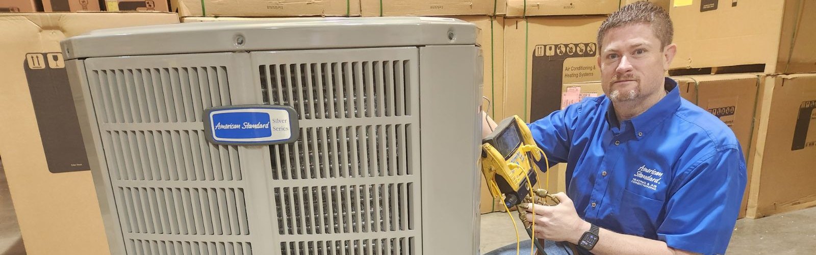Castle AC and Heating owner Josh Cartwright with refrigerant gauges beside an American Standard outdoor unit