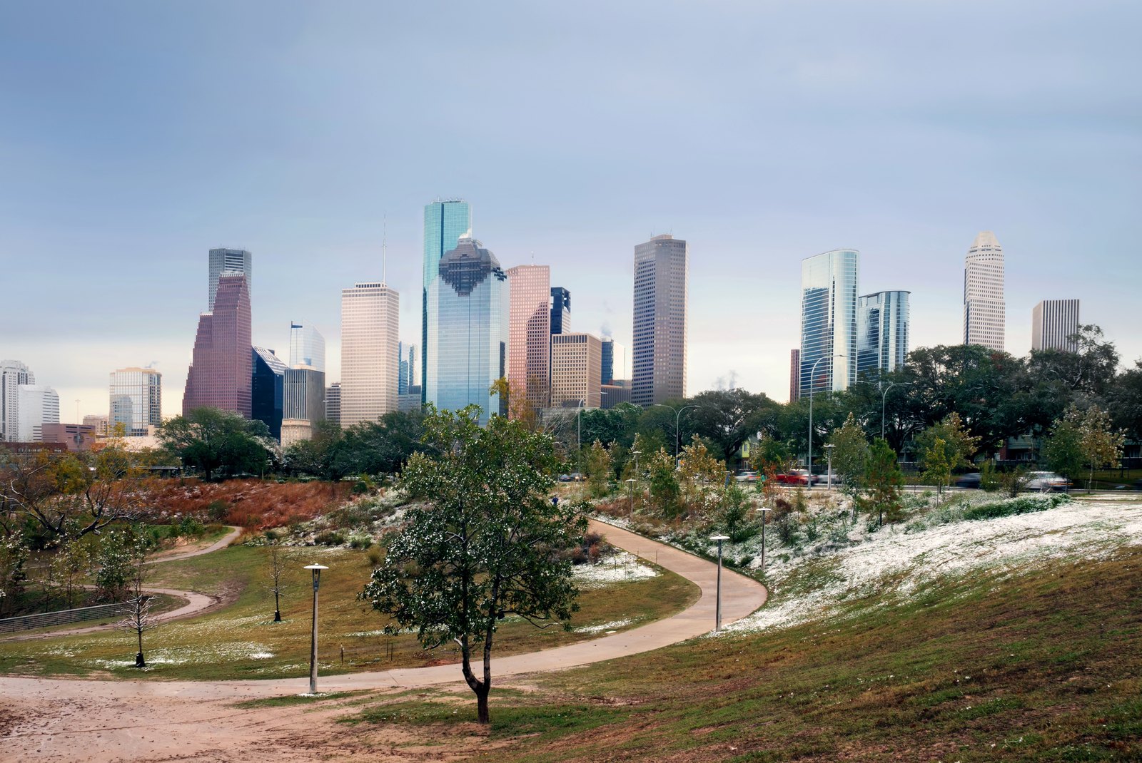 Snow lying on the ground in a Houston park during a winter freeze, with the downtown skyline in the background.
