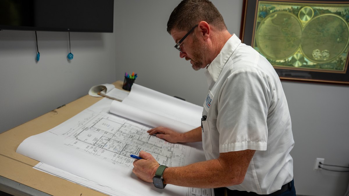 Castle technician measuring a Katy floor plan to size a replacement HVAC system